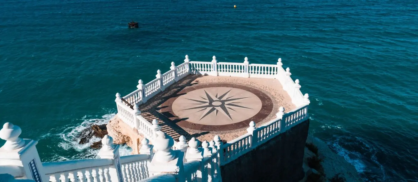 Mirador con balaustrada blanca y una gran rosa de los vientos de mosaico en el suelo, sobre un mar azul profundo