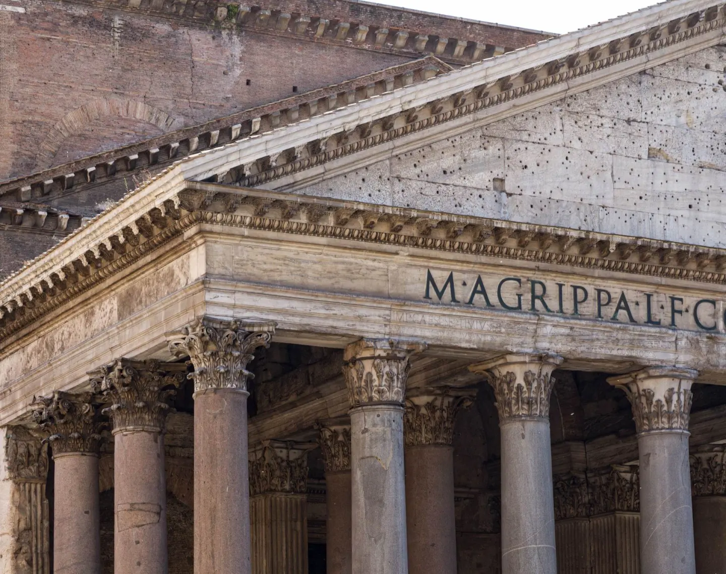 Pórtico de un templo antiguo con columnas de capiteles corintios de granito y un frontón con la inscripción «M·AGRIPPA·L·F·CO», con muros de ladrillo detrás