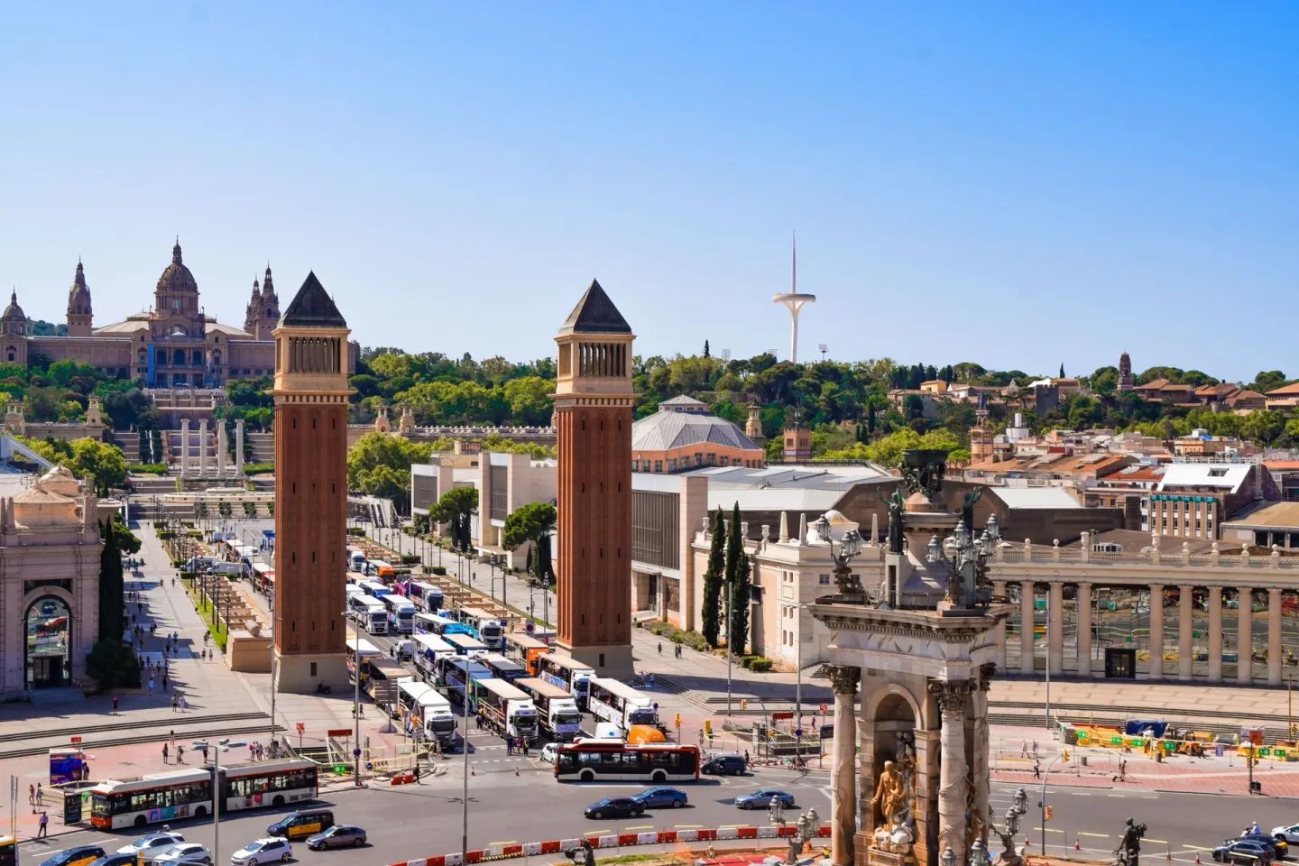 Dos torres de ladrillo en una plaza con mucho tráfico, con un gran edificio de cúpula y una torre blanca al fondo bajo un cielo azul