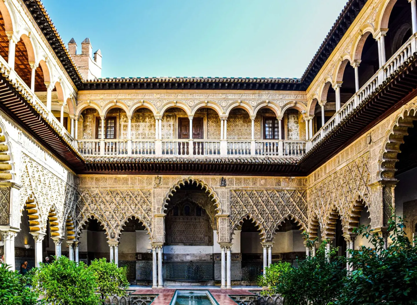 Patio de un palacio con arcos de herradura decorados con yeserías muy finas, una galería superior con balaustrada y naranjos en primer plano